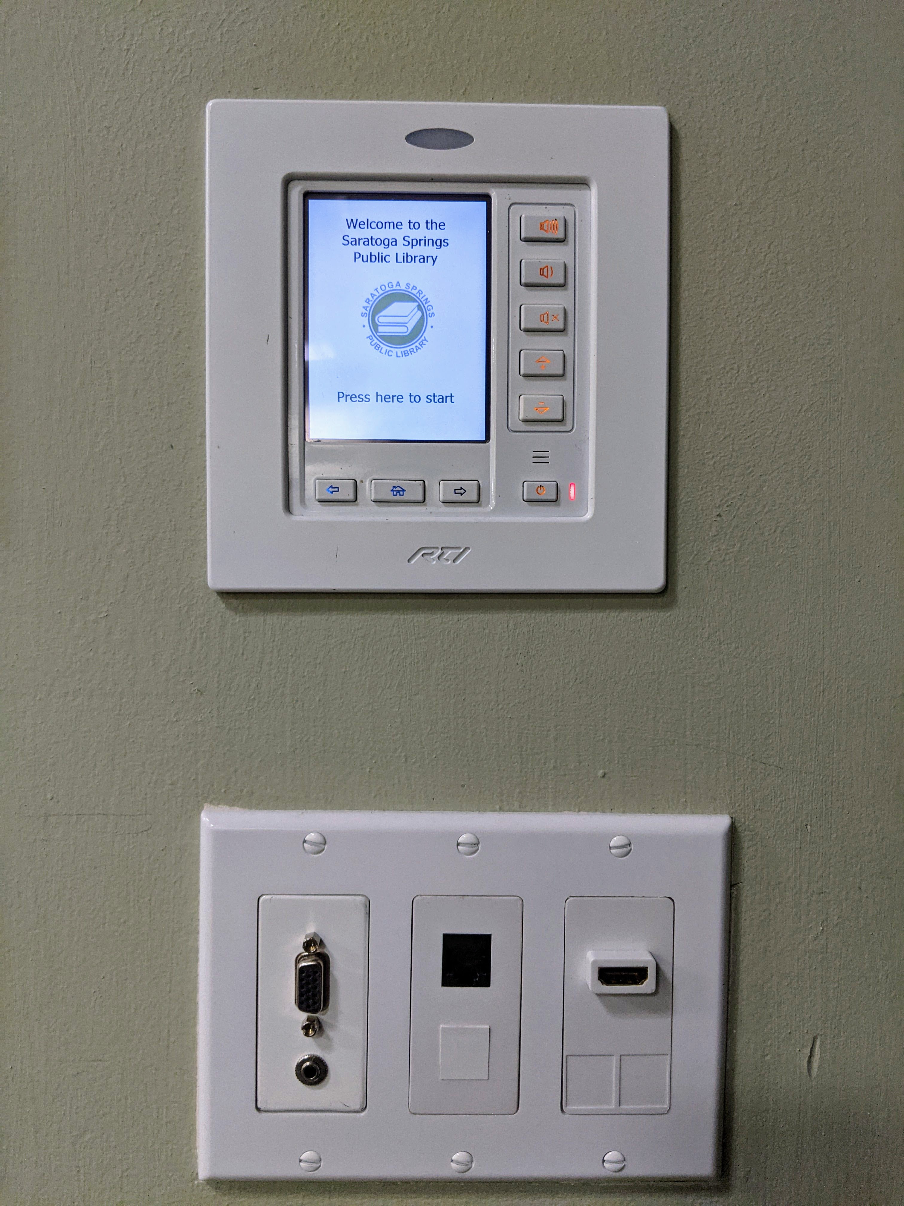 A touchscreen interface as part of a technology control panel for media connectivity. A panel below where physical connections can be made by devices to share media from.