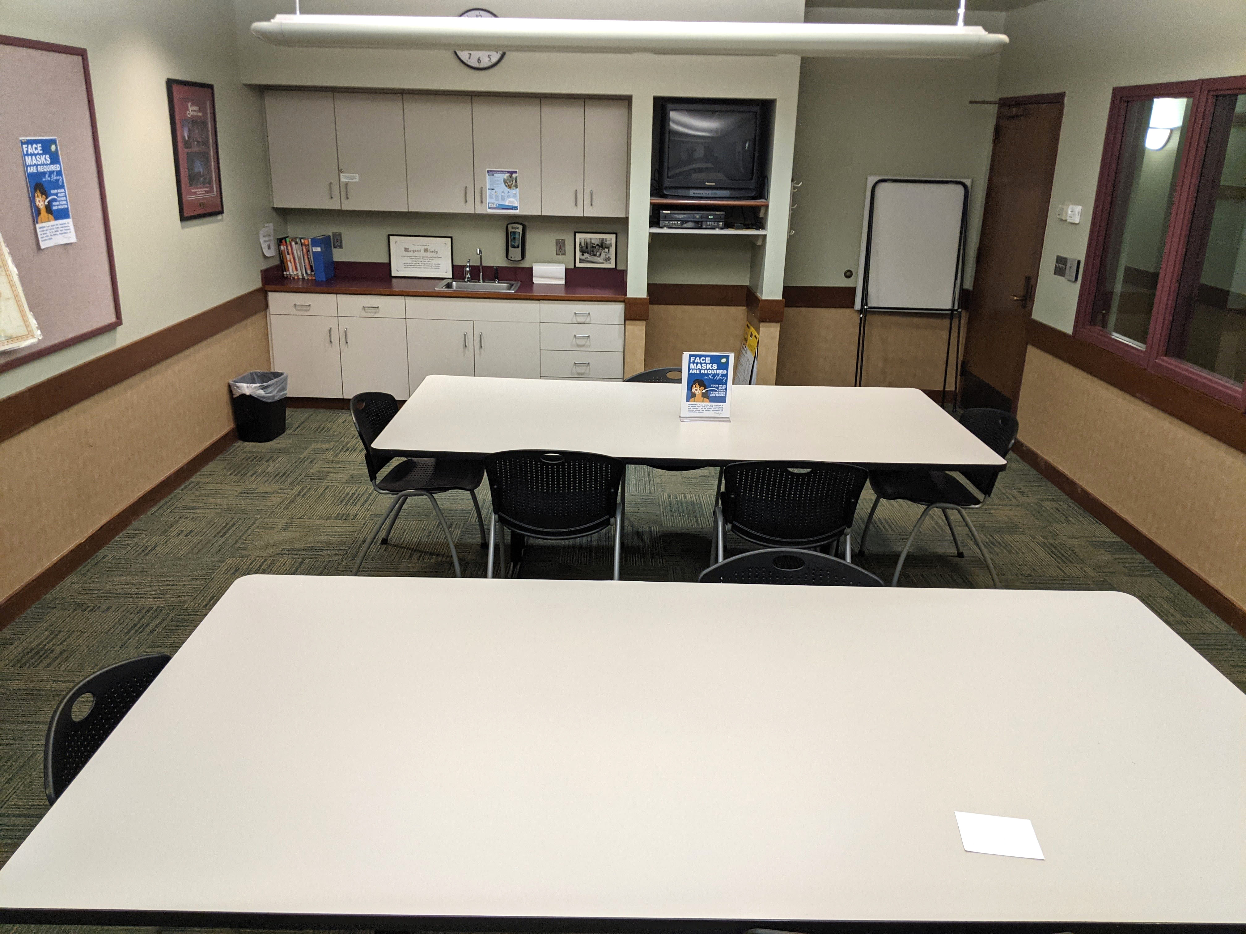 Tables and chairs showing the kitchenette at the far end of the room, looking towards the entry door.