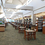 Thumbnail: A long floorspace with many evenly spaced tables set out in front of a long row of book shelving and high, open ceilings with natural light.