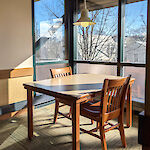 Thumbnail: A table with two chairs in an alcove with a single pendant light, and sinlight shining through the three sides of the alcove onto the table.