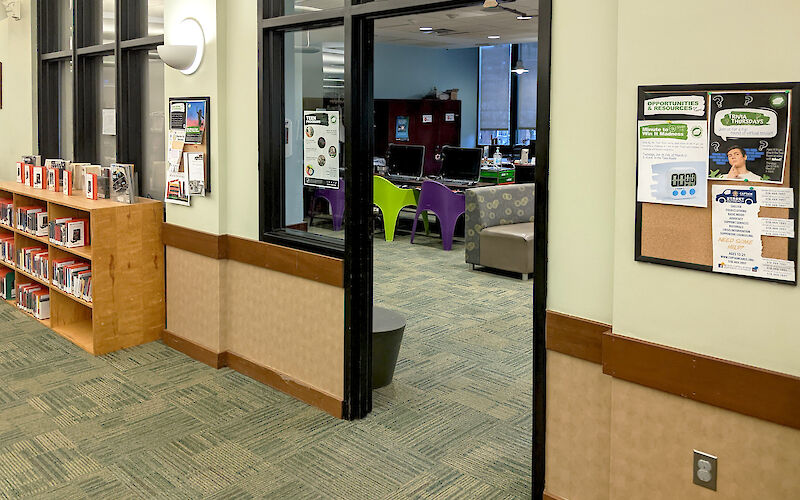 Open door peering into the Teen Room from the outside, showing part of a couch, colorful chairs, and computers.