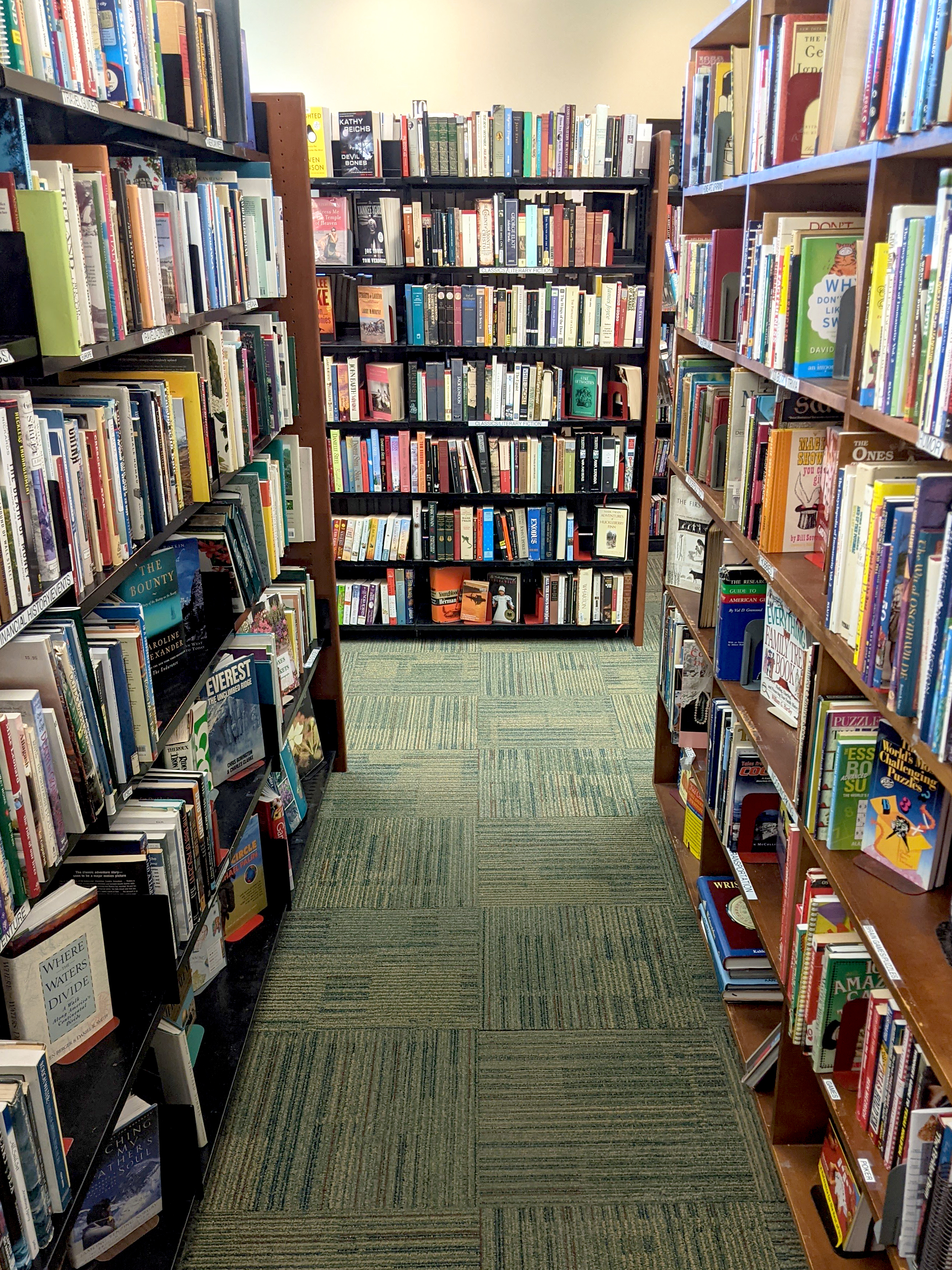 Full shelves of books looking down an aisle towards yet another shelf full of books at the end.