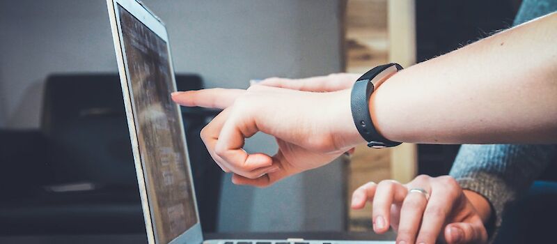 Close-up view of an opened laptop, two sets of hands reviewing what’s on the screen. Photo by John Schnobrich, Unsplash.