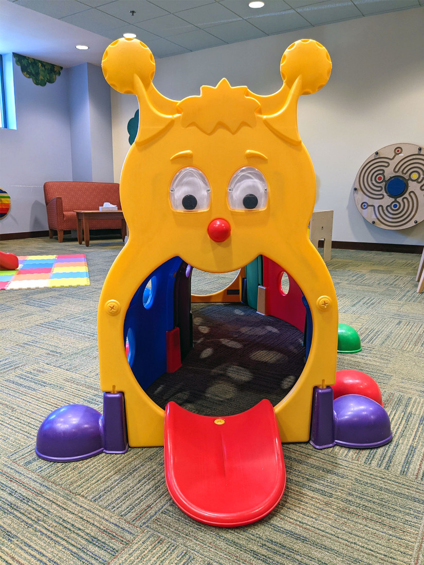 A wide, open-mouthed massive plastic caterpillar stares back, inviting children to crawl through the tunnel in its mouth’s opening.