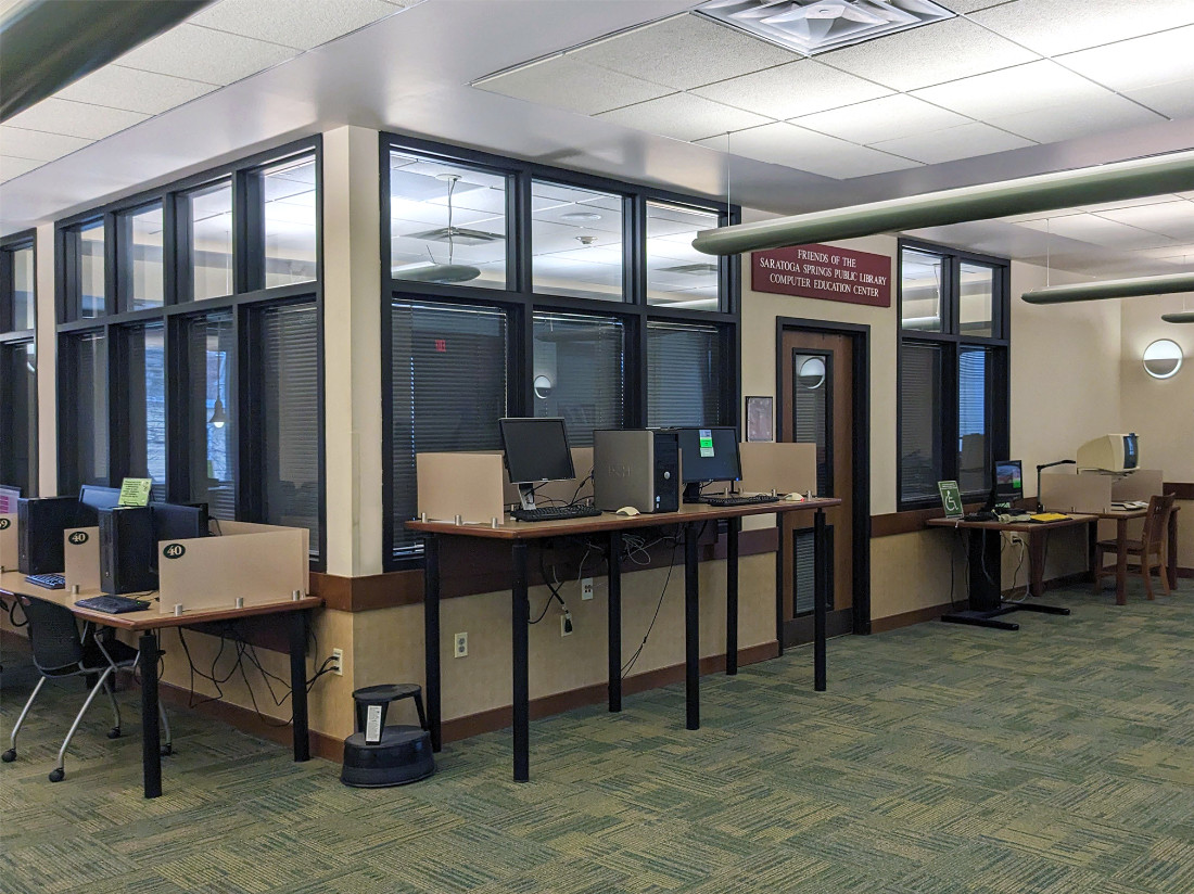 A doorway surrounded by 3 computers along a wall. Lights are on inside the room, with closed metal shades over the windows.