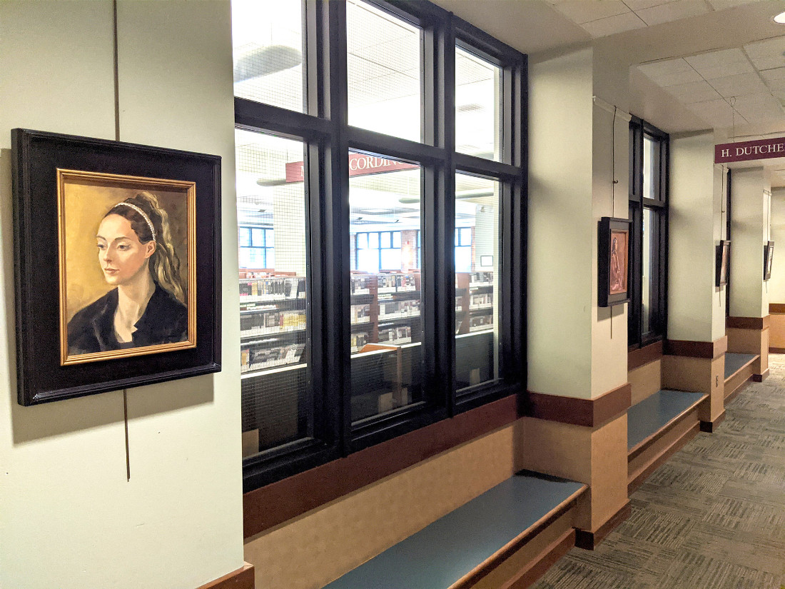 Images are hung on columns within a hallway. The nearest artwork is of a woman painted in period style, with a golden hue backdrop, brunette hair with golden highlights, and a black material around her shoulders.