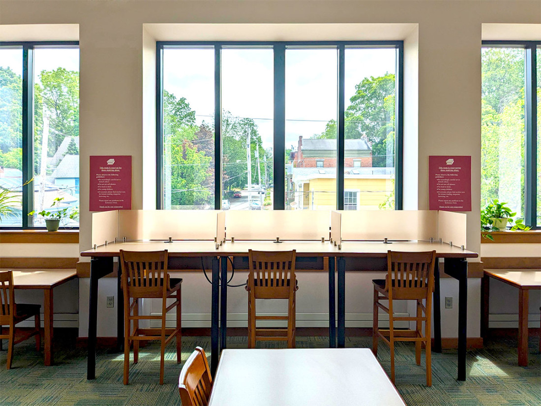 Three chairs at a long, sectioned table with a wide window overlooking the outside area with a single table and chair in the foreground.