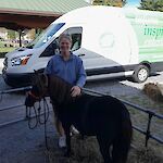 Thumbnail: A woman in a blue shirt standing outside with a brown miniature horse in front of a panel van with a library logo