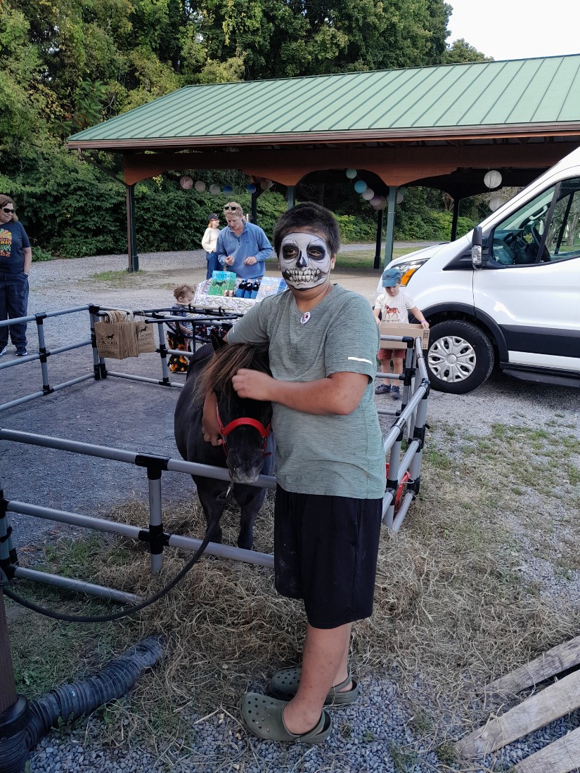 boy with skeleton painted face petting brown miniature horse outside